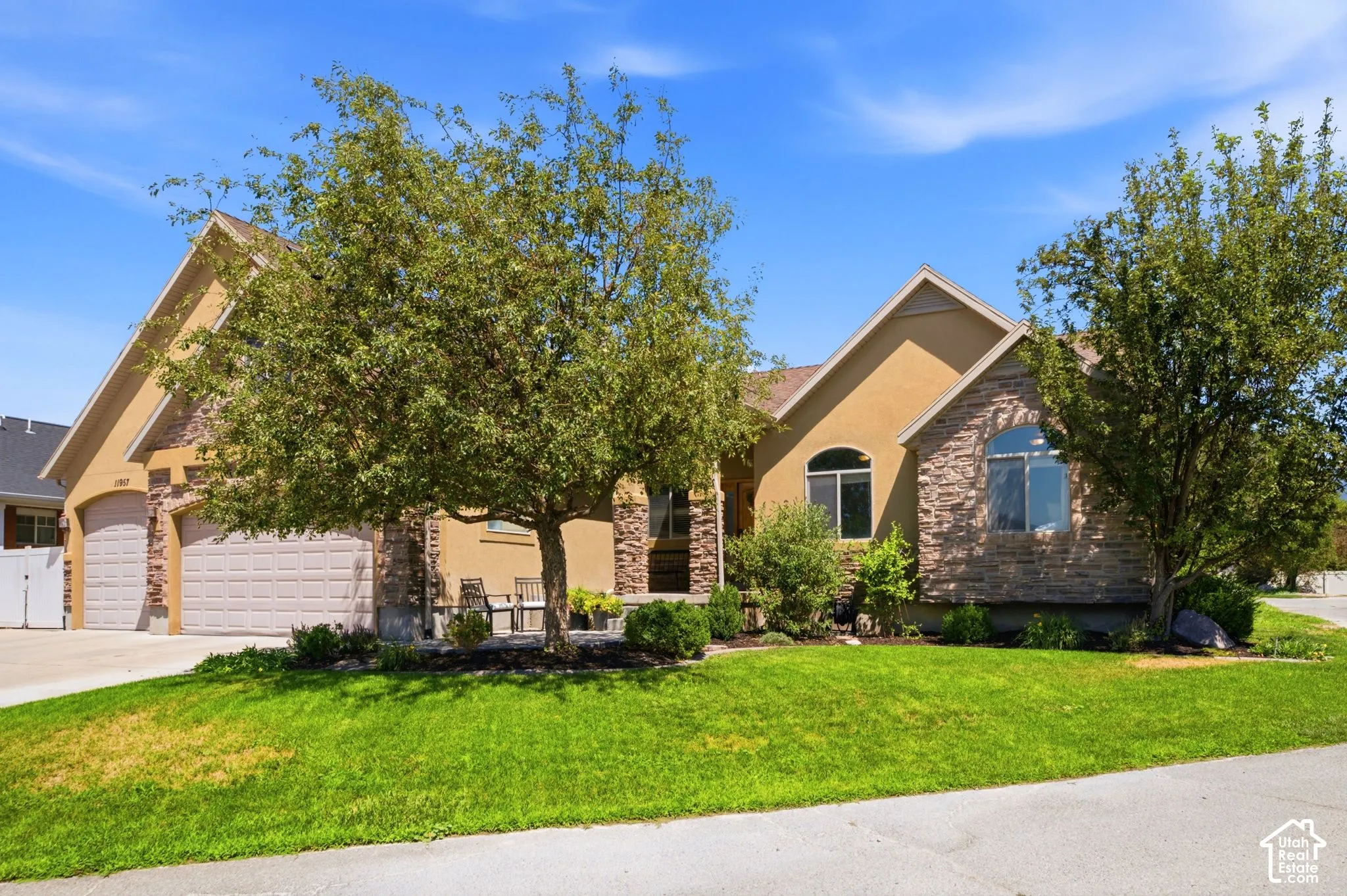 Stucco and stone facade home featuring a two-car garage, arched windows, and mature landscaping
