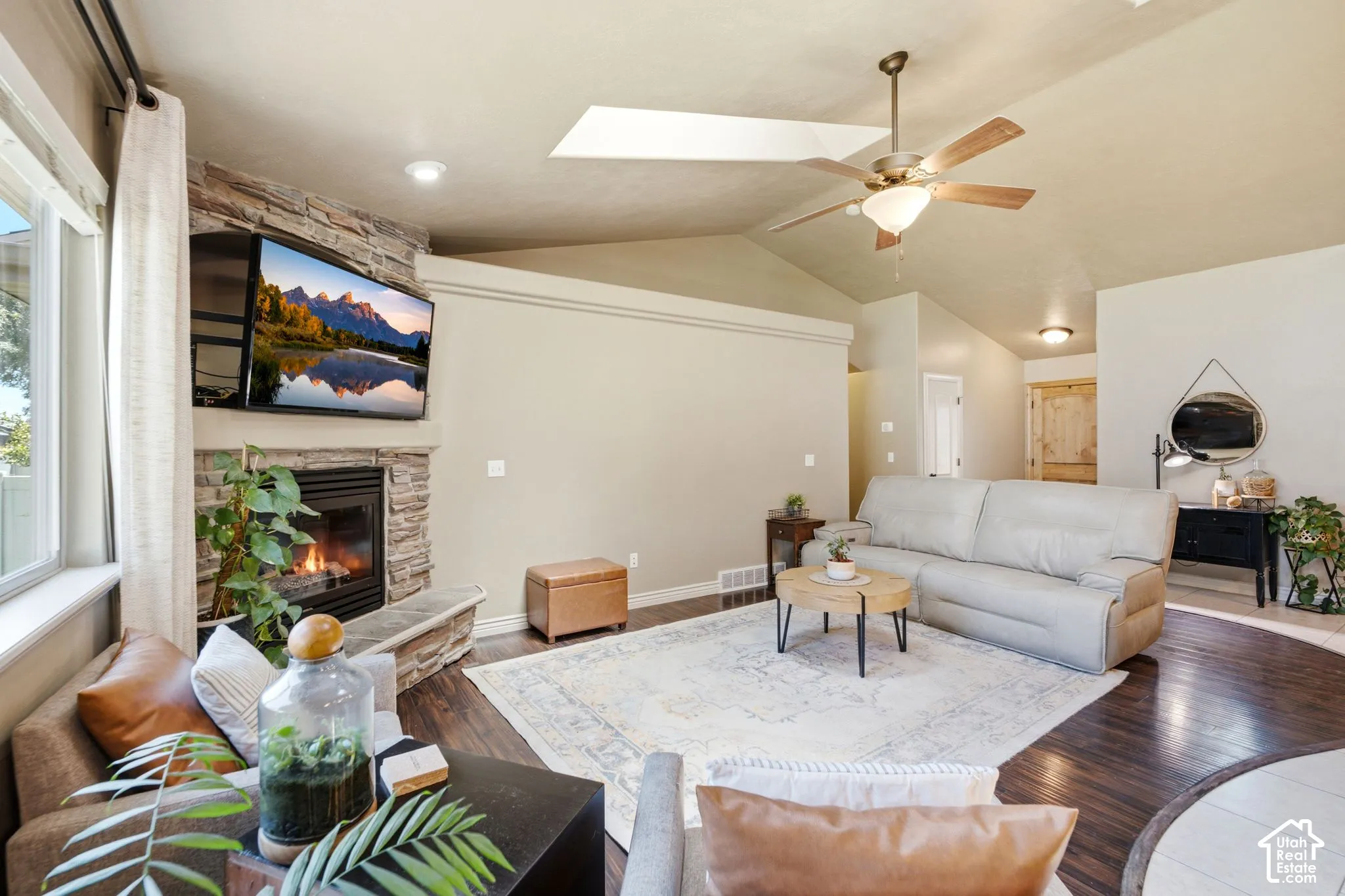 Living room featuring a stone-clad fireplace with hearth, vaulted ceilings, and dark wood-finish flooring