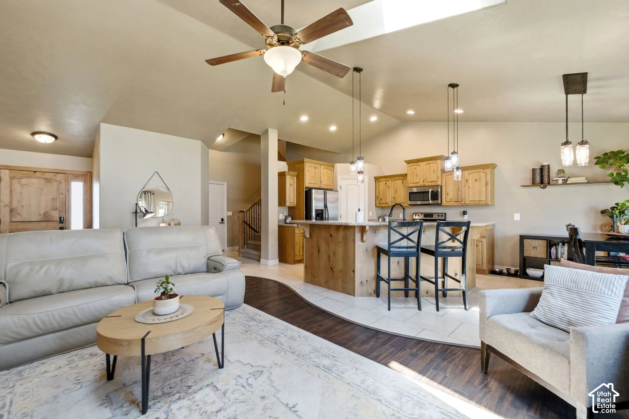 Living area with vaulted ceilings and a skylight, featuring wood-finish flooring and a ceiling fan