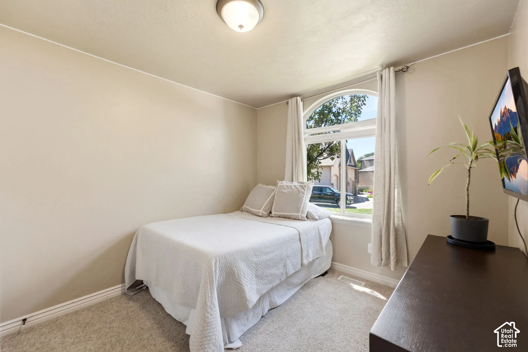Bedroom featuring a large arched window with white trim, light beige walls, and neutral-toned carpeting
