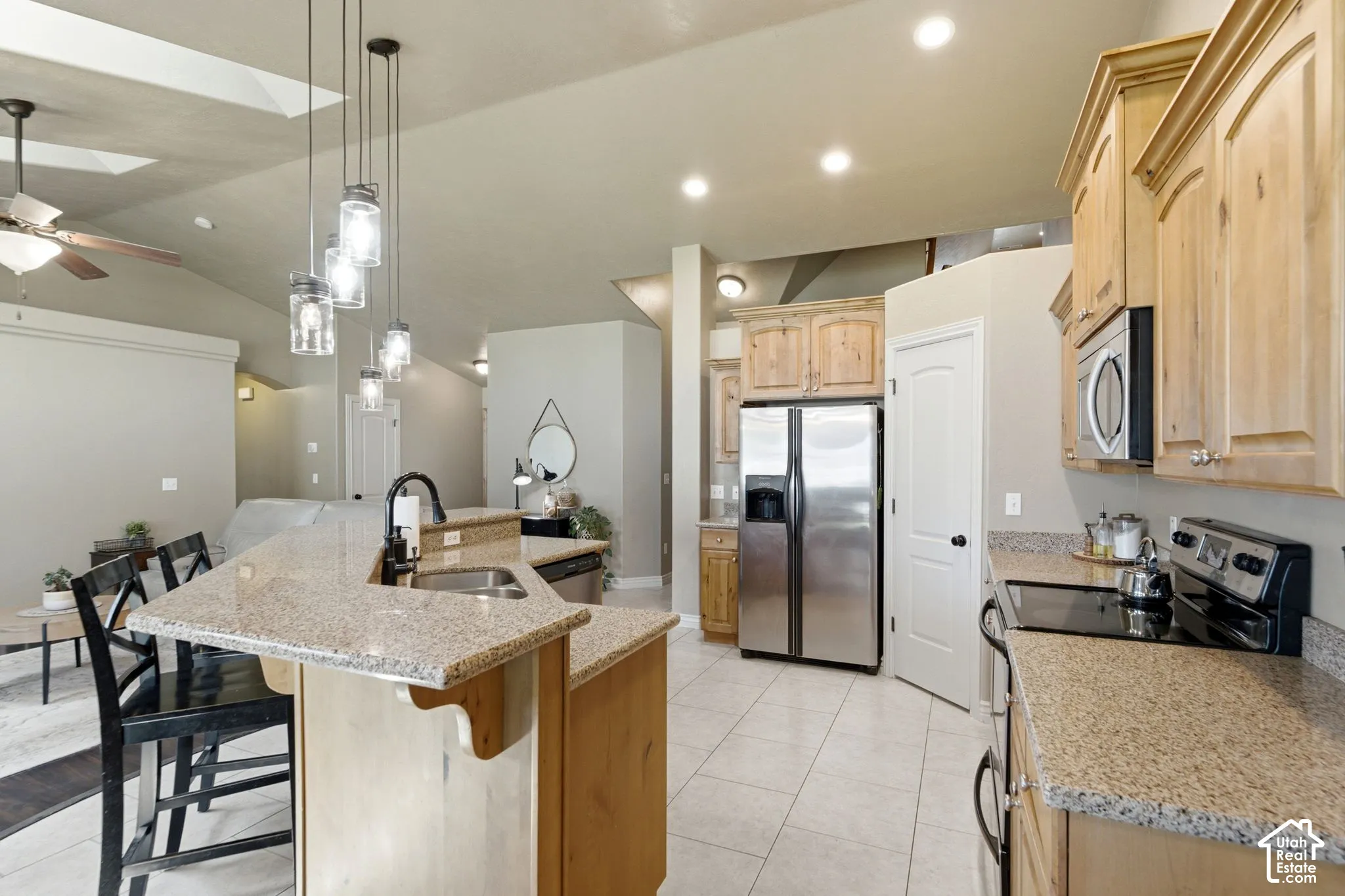 Kitchen featuring light wood cabinetry, speckled countertops, stainless steel appliances, and tile flooring