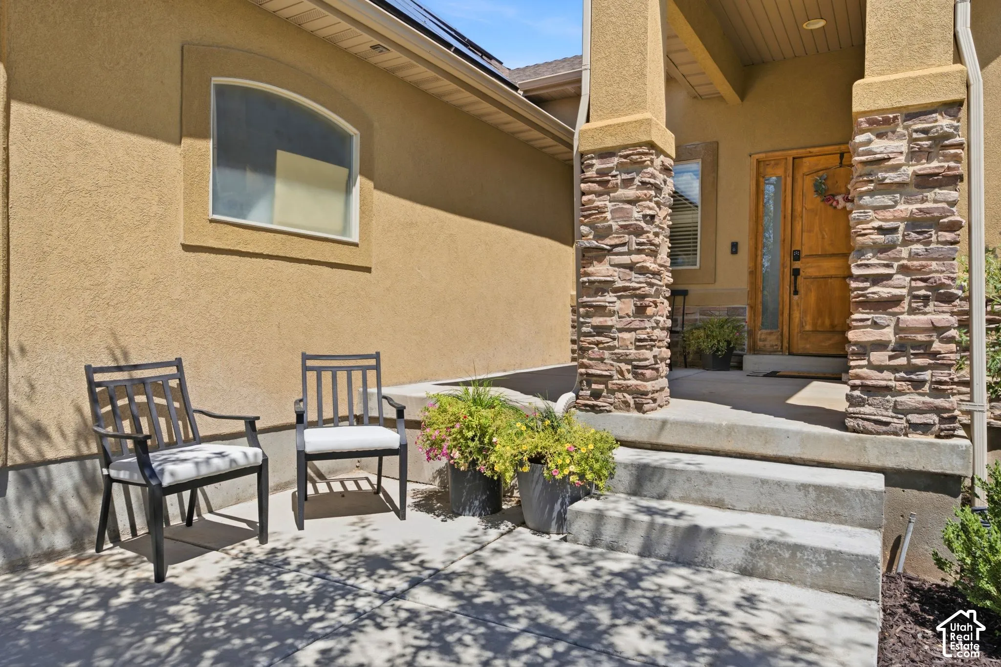 Stucco exterior featuring stacked stone columns, a solid wood entry door with vertical glass insert, and concrete steps leading to the front porch