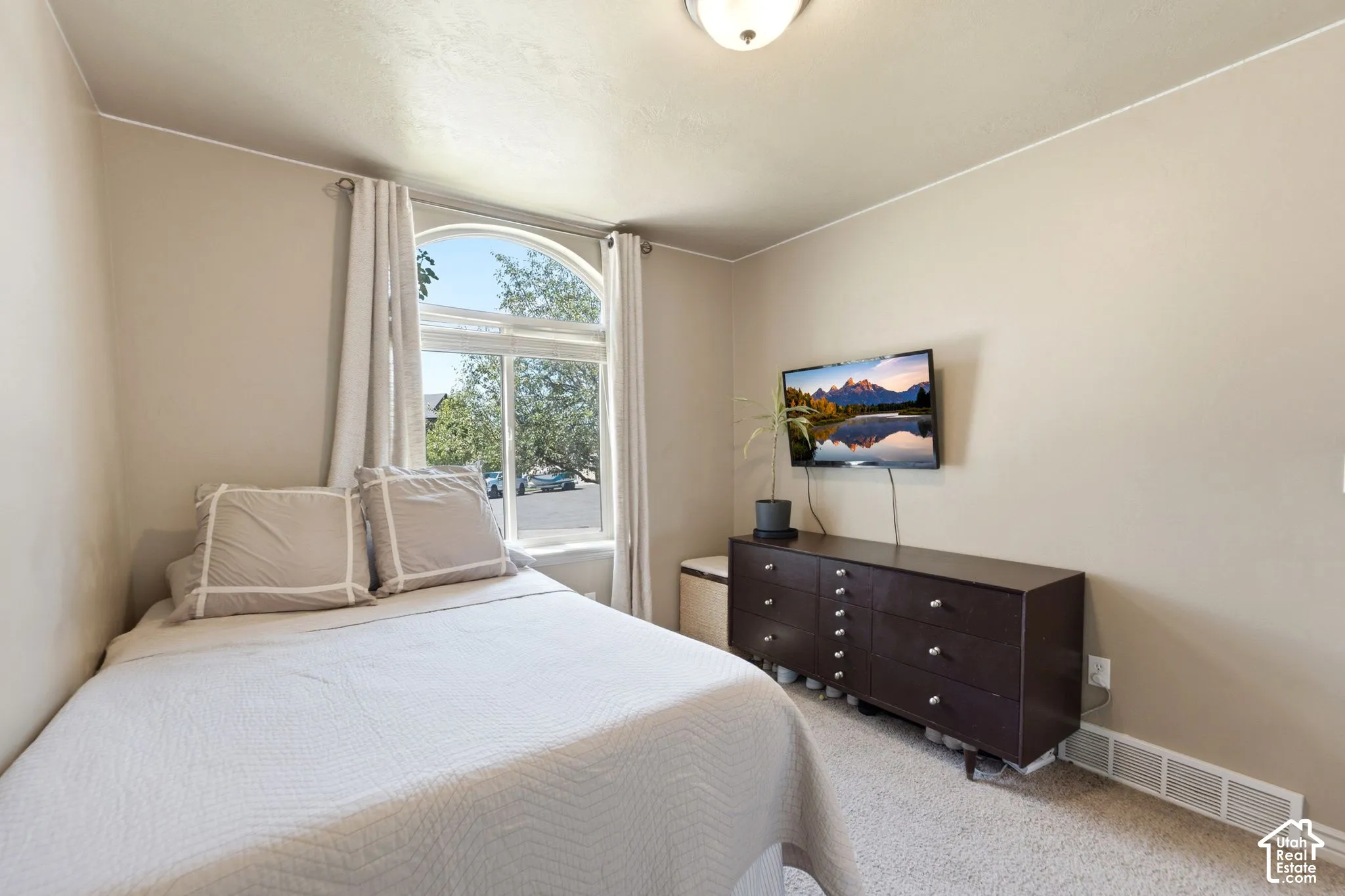 Bedroom featuring an arched window with white trim, neutral wall color, and light-colored carpet flooring
