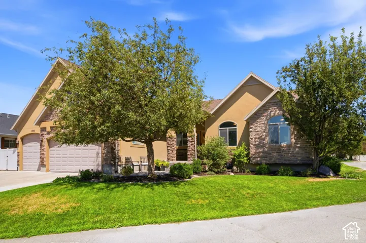 Stucco and stone facade home featuring a two-car garage, arched windows, and mature landscaping