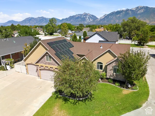 Property featuring a multi-panel solar array, stone and stucco exterior, an attached multi-car garage, and a manicured front lawn