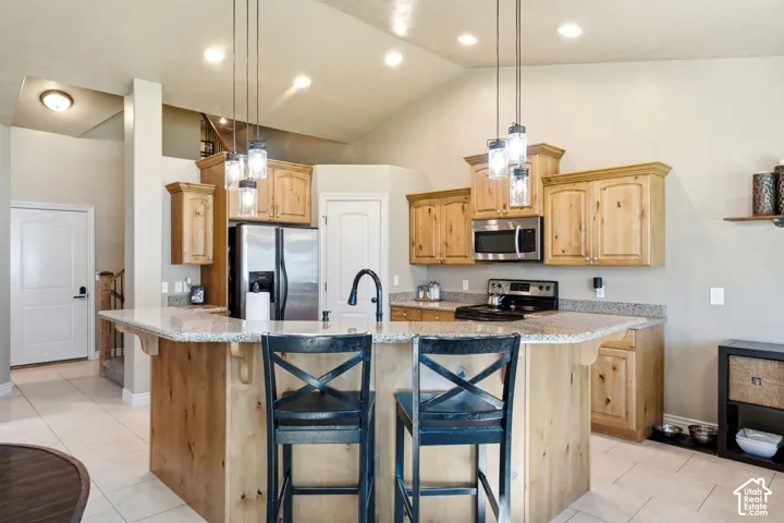 Kitchen featuring a peninsula island with bar seating, light wood cabinetry, stone-finish countertops, stainless steel appliances, and tile flooring