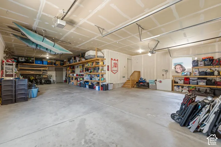 Spacious garage featuring a concrete floor, built-in shelving, and a stairway with wood handrails