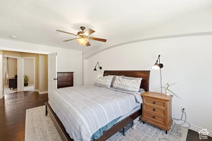 Spacious room featuring dark wood-finish flooring, a ceiling fan with light fixture, white walls, and an arched wall detail
