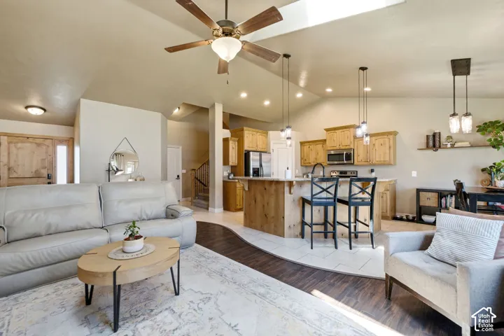 Living area with vaulted ceilings and a skylight, featuring wood-finish flooring and a ceiling fan