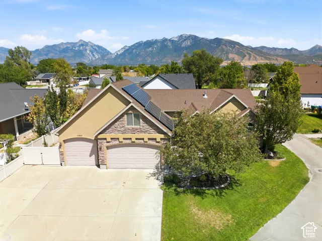 Mountain backdrop, attached two-car garage, stone and stucco exterior, solar panel installation, paved driveway