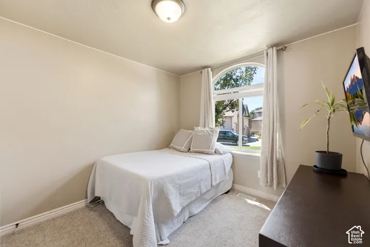 Bedroom featuring a large arched window with white trim, light beige walls, and neutral-toned carpeting