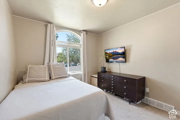Bedroom featuring an arched window with white trim, neutral wall color, and light-colored carpet flooring