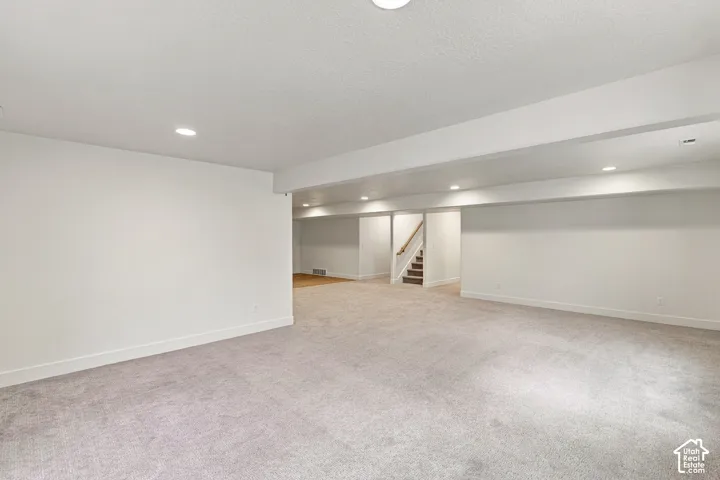 Recessed lighting, light-toned carpeting, white painted walls, wood-finish flooring, and a staircase with a wood handrail