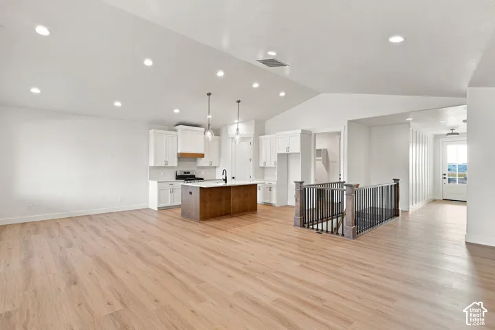 Vaulted ceiling, recessed lighting, wood-finish flooring, white cabinetry, and a kitchen island with pendant lighting