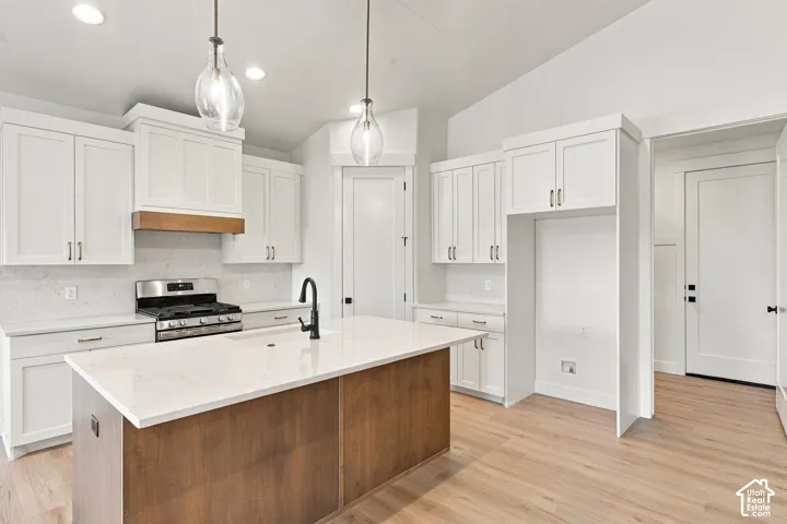 Kitchen featuring white shaker cabinetry, an island with a light-toned countertop, a stainless steel range, and wood-finish flooring