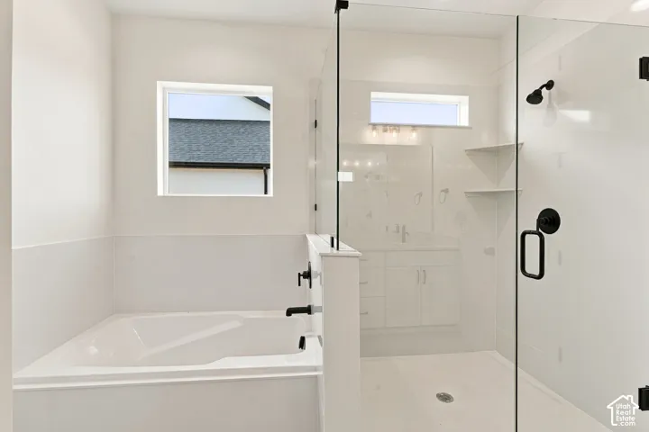 Soaking tub with matte black fixtures, adjacent to a glass-enclosed shower with matte black hardware, built-in shelving, and a vanity visible in the background