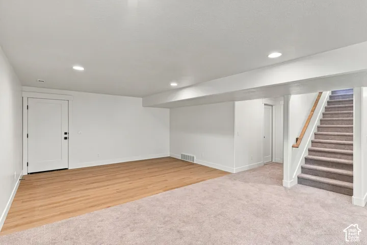 Recessed lighting, wood-finish flooring, carpeted area, white paneled doors, and a carpeted staircase with a wood handrail
