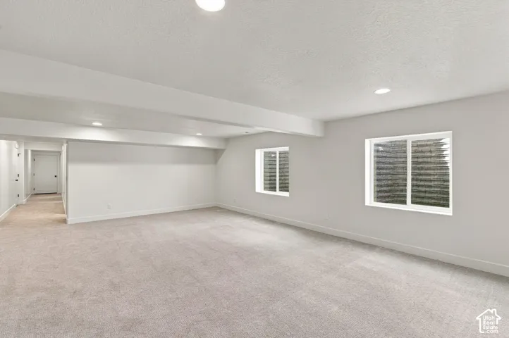 Spacious room with light-colored carpeting, two egress windows, recessed lighting, and a white paneled door