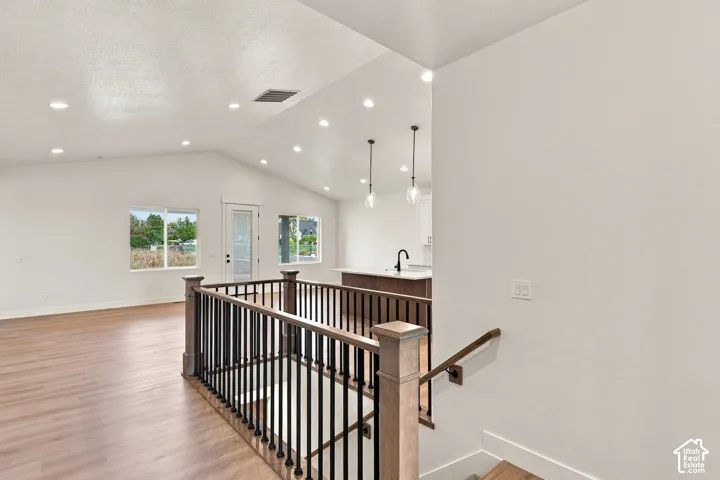 Vaulted ceiling with recessed lighting, wood-finish flooring, and a kitchen island with pendant lighting