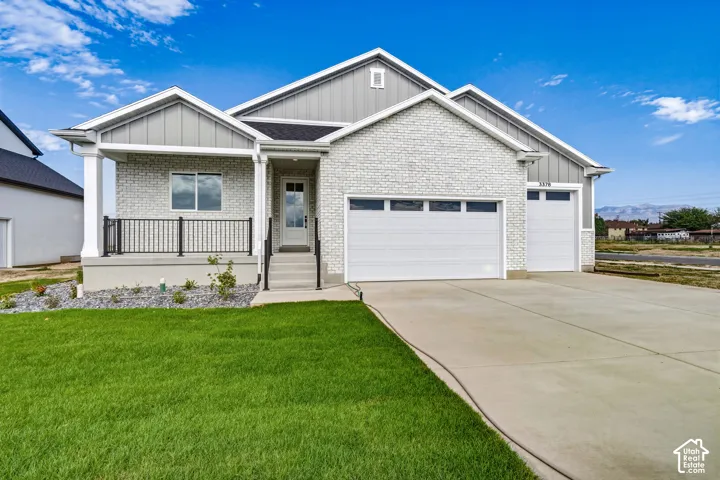 White brick exterior with gray siding accents, two-car garage, covered porch with black railings, concrete driveway, and a manicured lawn