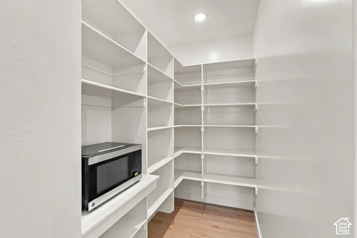 Spacious pantry featuring extensive white shelving, wood-finish flooring, and recessed lighting