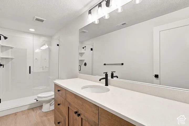 Wood-finish flooring, a wood vanity with a white countertop, an integrated sink, a large mirror, and a walk-in shower with a glass enclosure