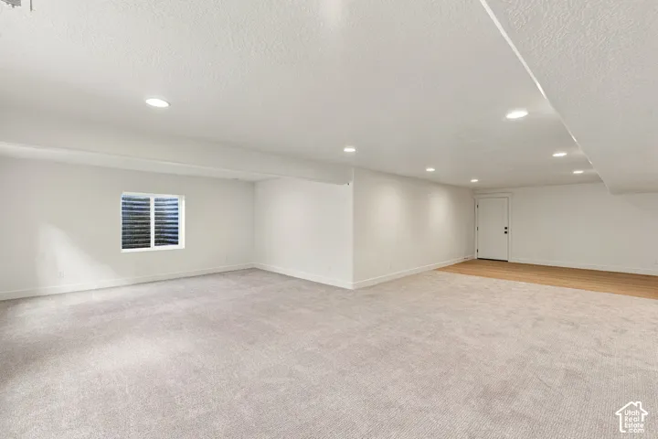 Expansive room featuring recessed lighting, a window with horizontal blinds, light-toned carpeting, and wood-finish flooring