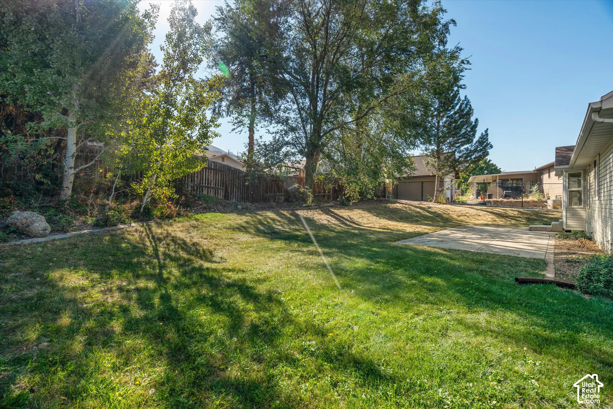 Expansive lawn area with mature trees, established landscaping, and a concrete patio