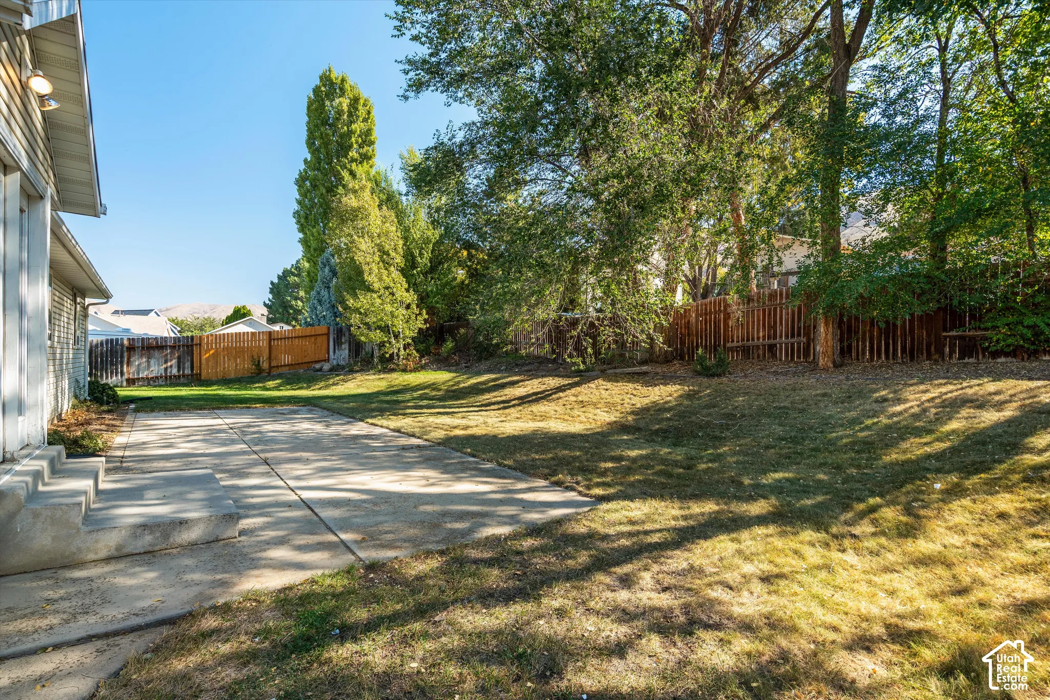 Expansive yard with mature trees, a concrete patio, and slatted wood fencing