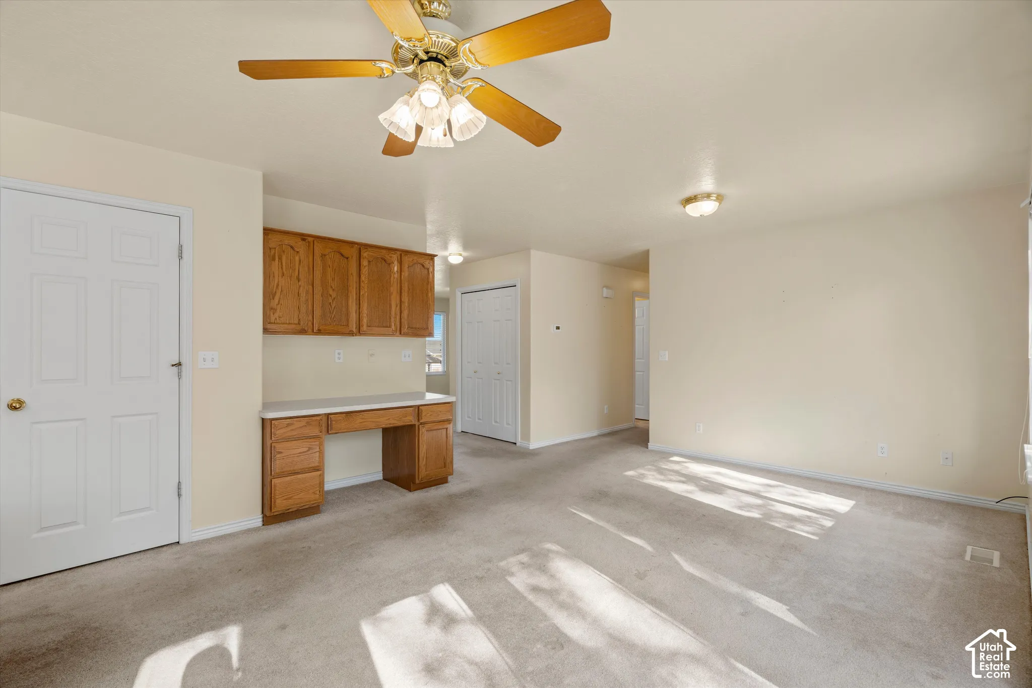 Built-in desk with overhead cabinetry, ceiling fan with light fixture, flush mount ceiling lights, and light-toned carpeting