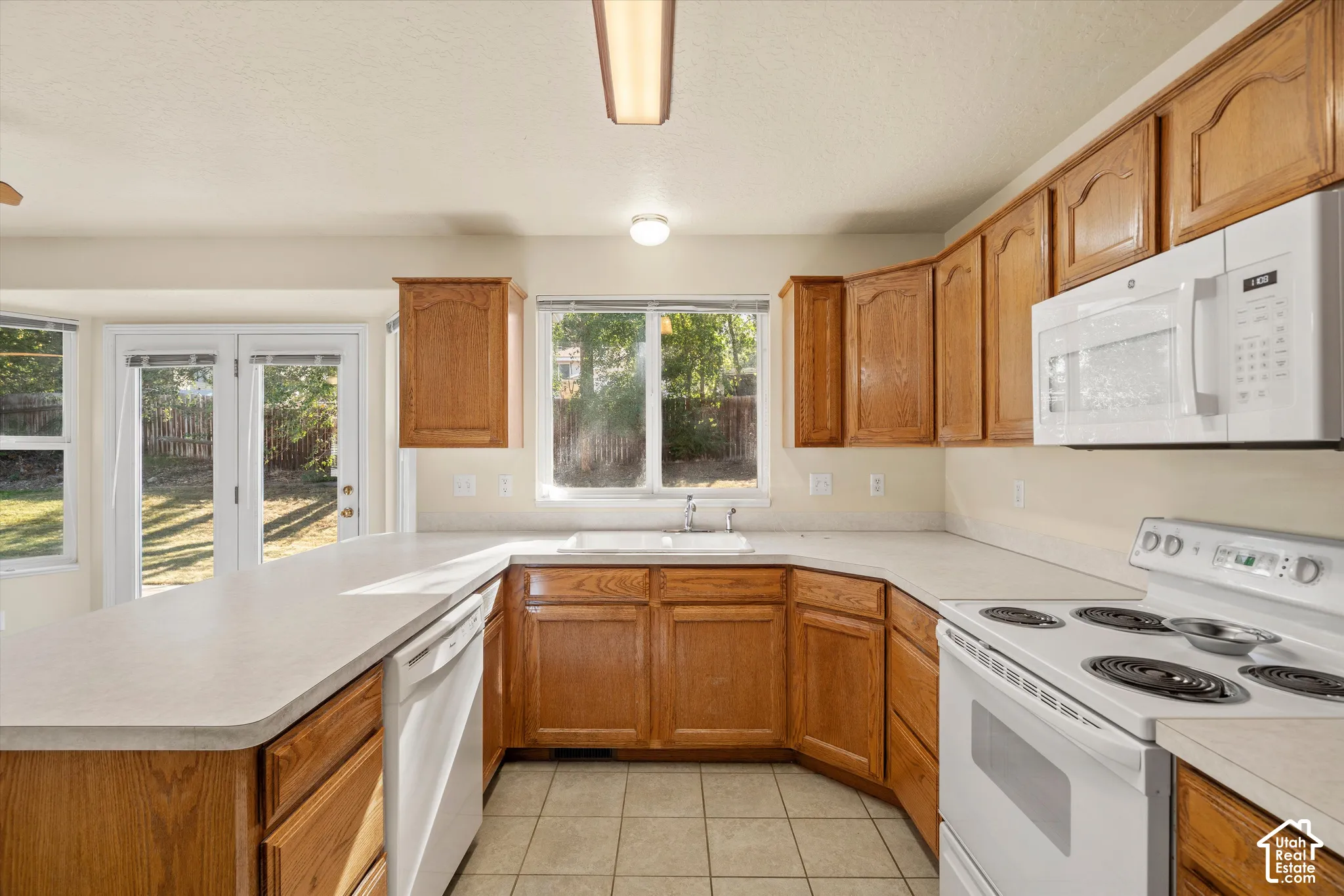 Kitchen featuring wood cabinetry, white appliances, solid surface countertops, and tile flooring
