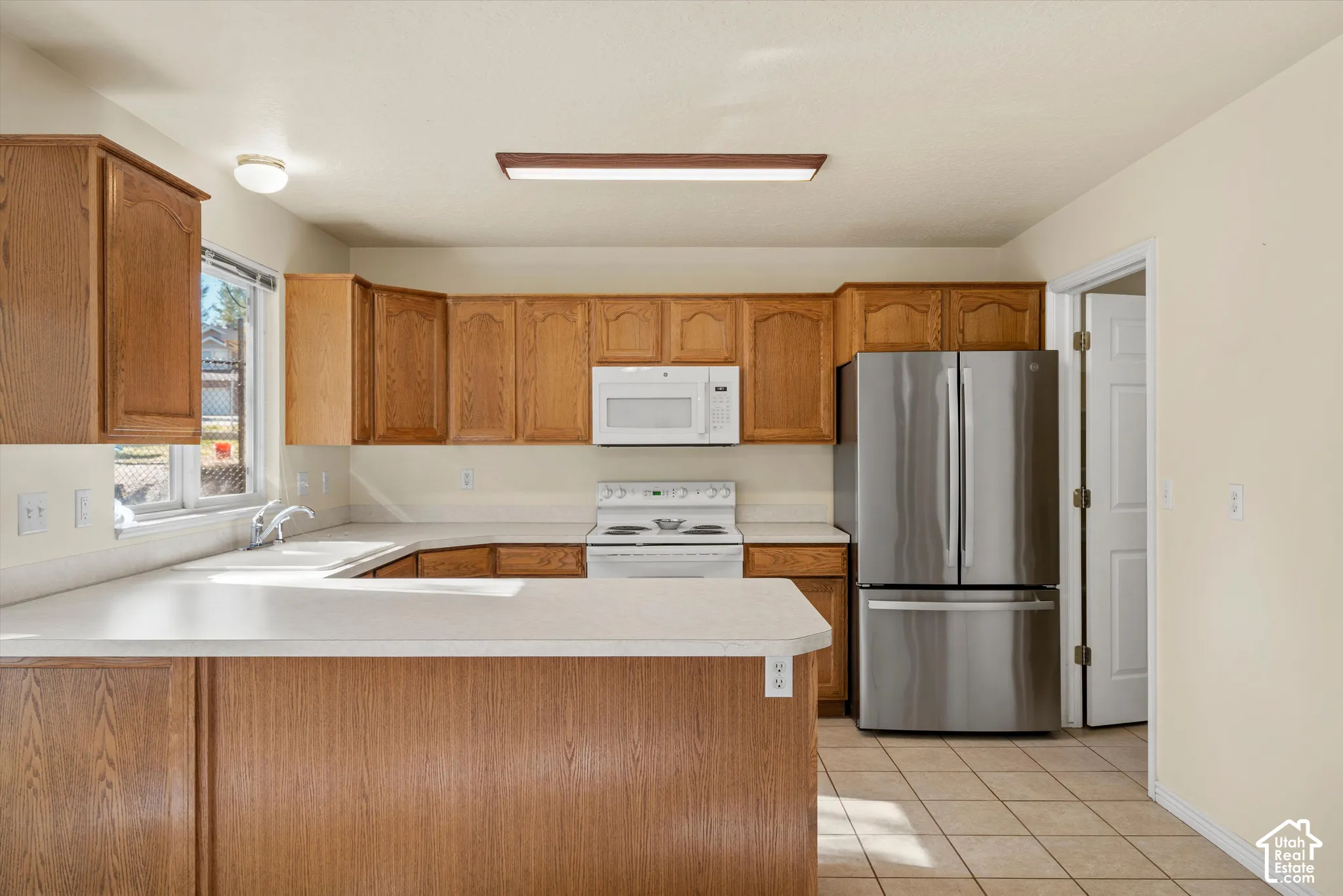 Kitchen featuring wood cabinetry, white countertops, stainless steel refrigerator, white microwave, and white electric range