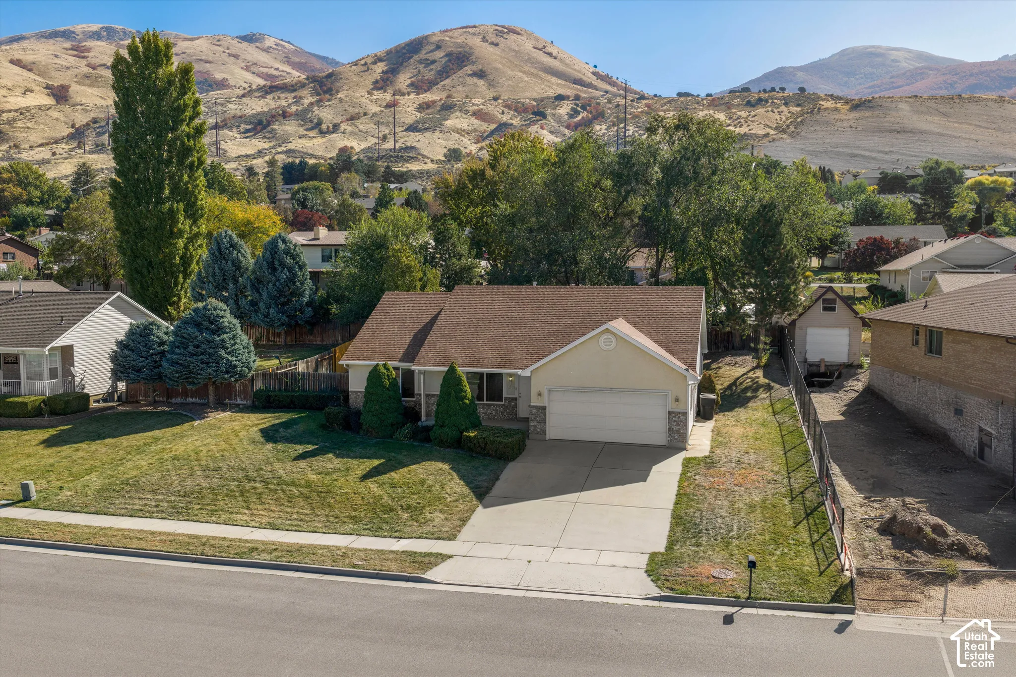 Siding exterior with stone accents, attached garage, paved driveway, landscaped front yard, and a mountain backdrop