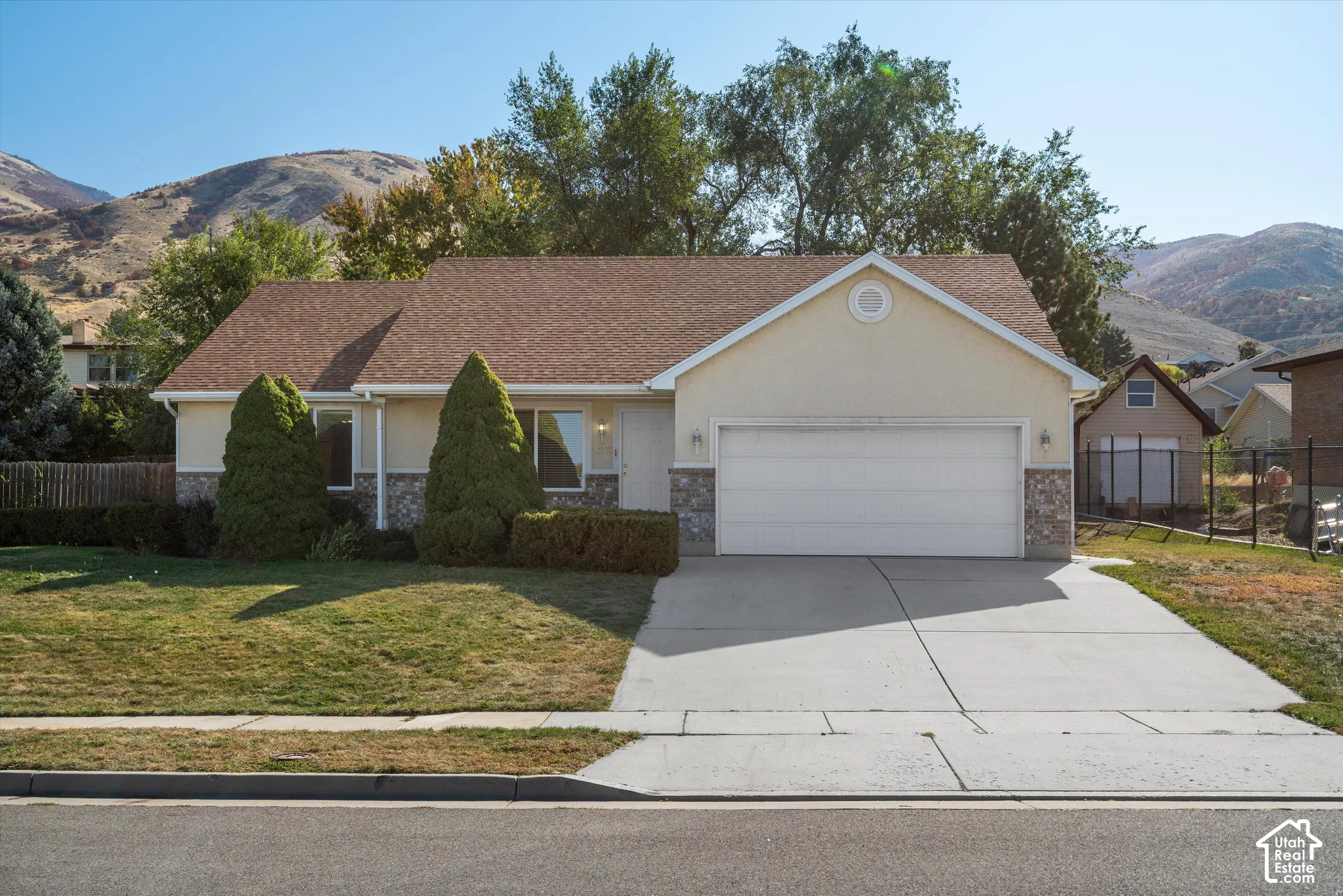 Light-colored stucco exterior with stone accents, attached two-car garage, concrete driveway, and front lawn with mature landscaping
