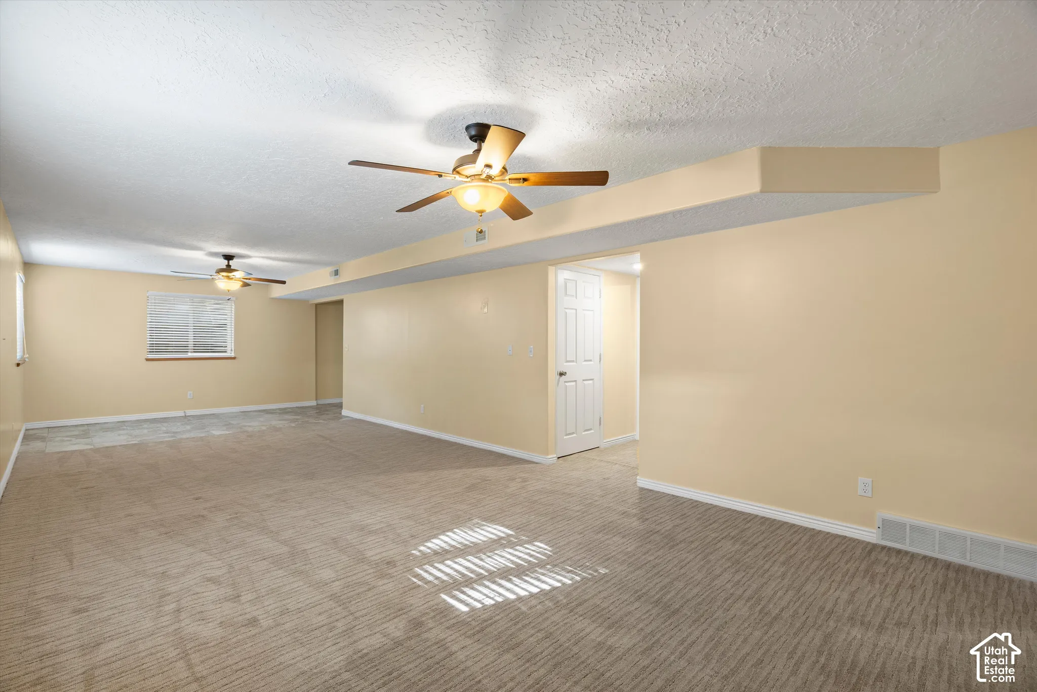 Spacious room featuring carpeting, ceiling fans with integrated lighting, and multiple windows with blinds