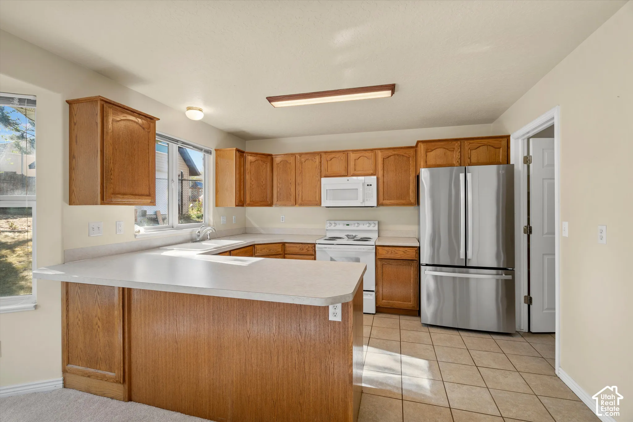 Kitchen featuring wood cabinetry, light-toned countertops, white appliances, stainless steel refrigerator, and tiled flooring