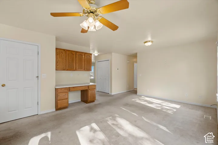 Built-in desk with overhead cabinetry, ceiling fan with light fixture, flush mount ceiling lights, and light-toned carpeting