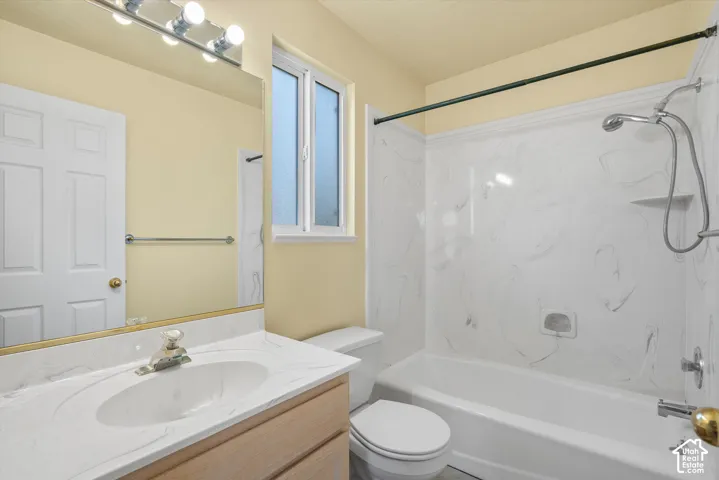 Bathroom featuring a single vanity with an integrated sink, a built-in mirror with overhead lighting, a shower-over-tub combination with a white surround, and a privacy window