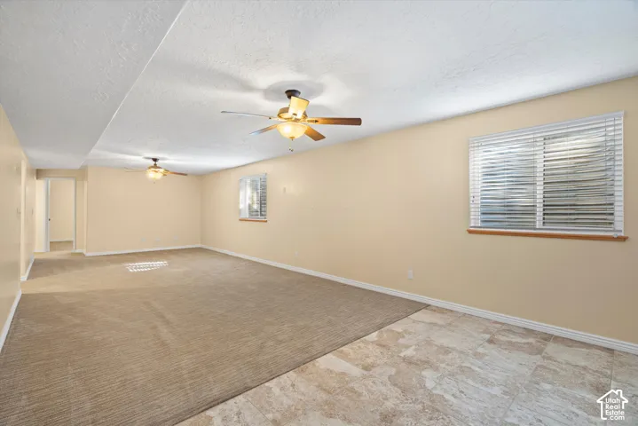 Expansive room featuring carpet and tile flooring, multiple ceiling fans, and natural light from a window with blinds