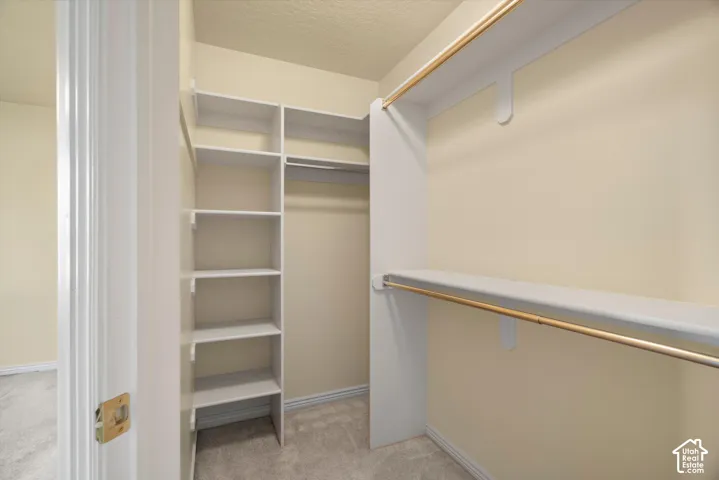 Walk-in closet with built-in shelving, two hanging rods, and light-toned carpeting