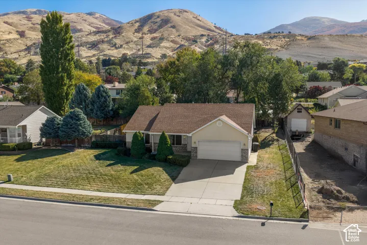 Siding exterior with stone accents, attached garage, paved driveway, landscaped front yard, and a mountain backdrop