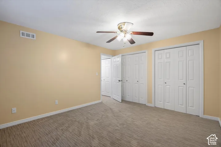 Carpeted room with a ceiling fan, two sets of bifold closet doors, and light-colored walls