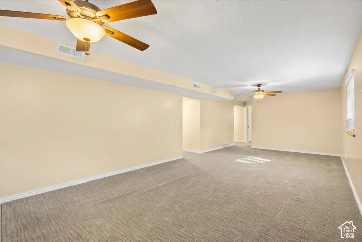 Spacious room featuring ceiling fans with integrated lighting, textured carpeting, and light-colored wall finishes