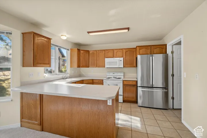 Kitchen featuring wood cabinetry, light-toned countertops, white appliances, stainless steel refrigerator, and tiled flooring