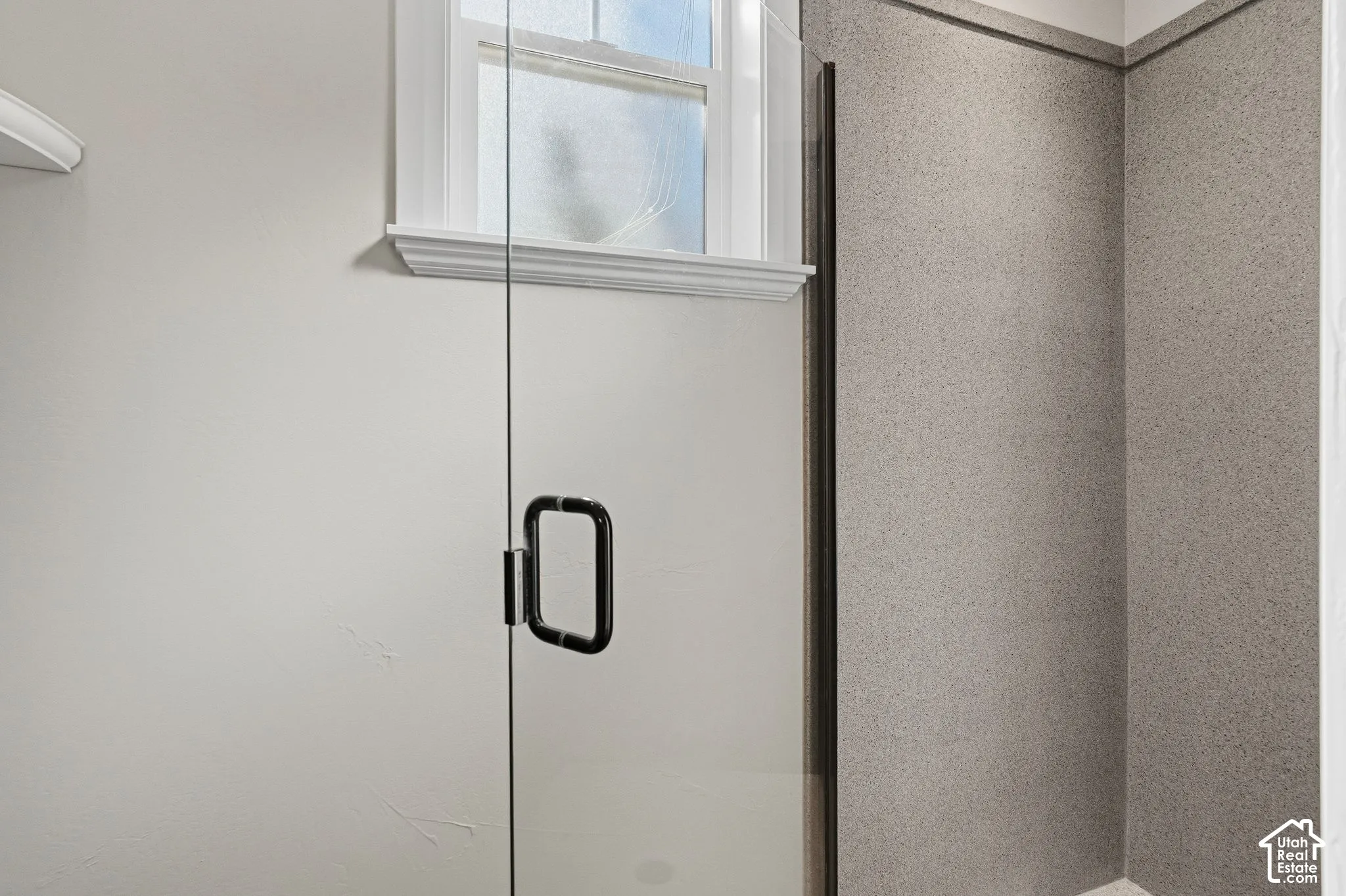 Frameless glass shower enclosure with a matte black handle and textured wall panels