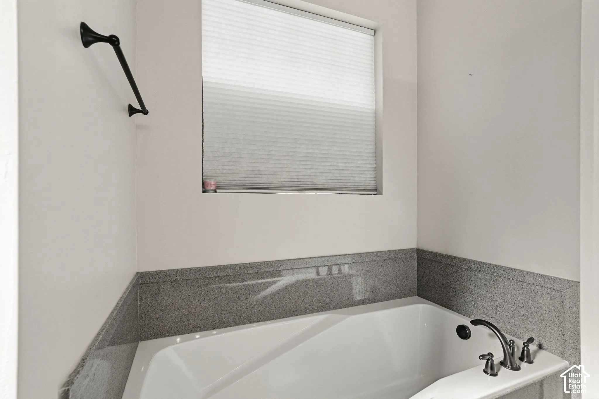 White soaking tub with dark bronze fixtures and a surrounding gray stone-look finish