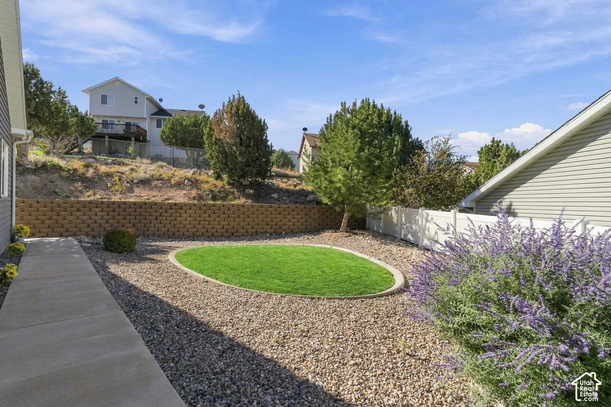 Landscaped exterior featuring a concrete walkway, gravel ground cover, a retaining wall, and a white privacy fence