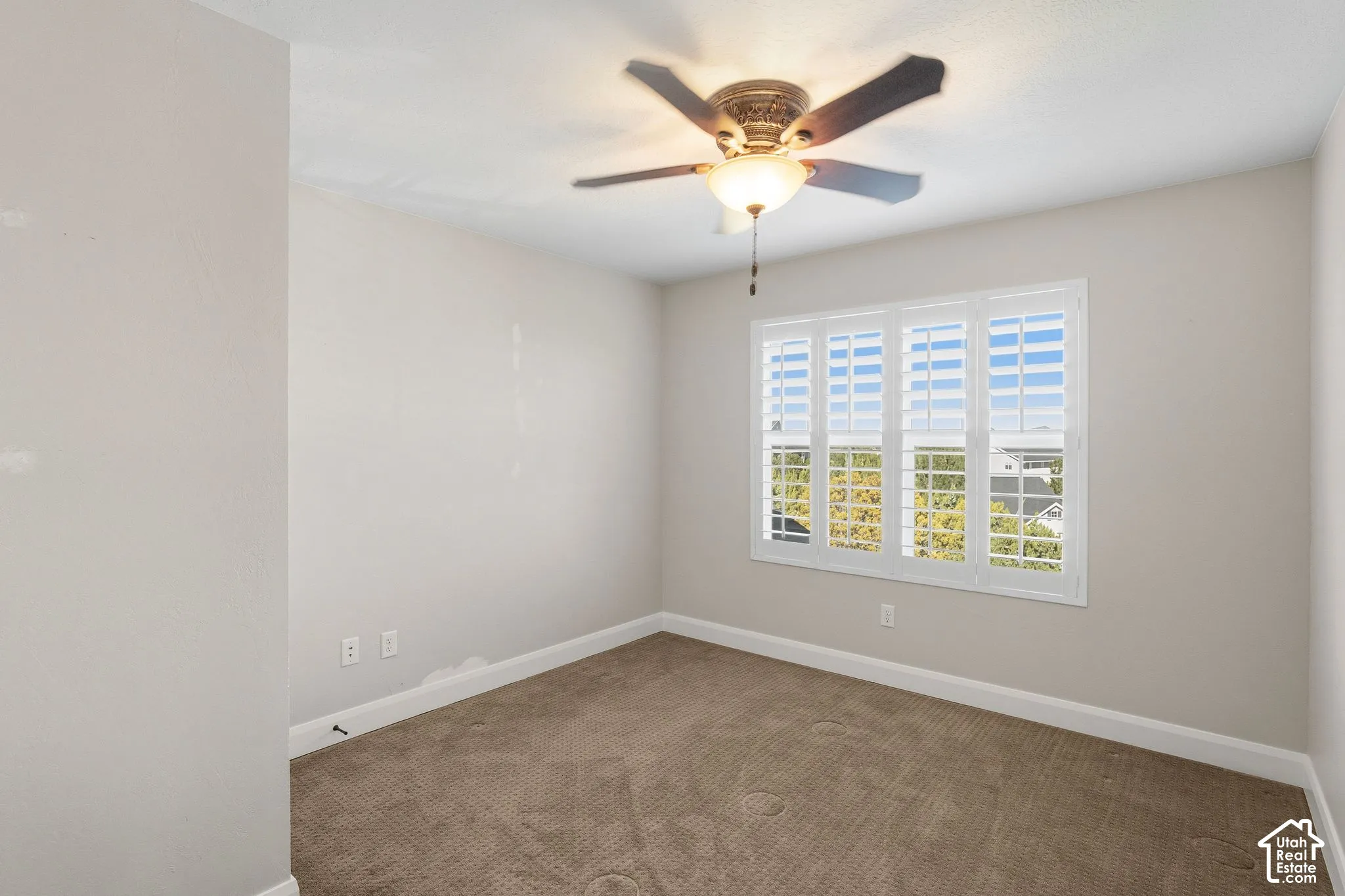 Ceiling fan with integrated lighting, window with plantation shutters, neutral-toned walls, and carpet flooring