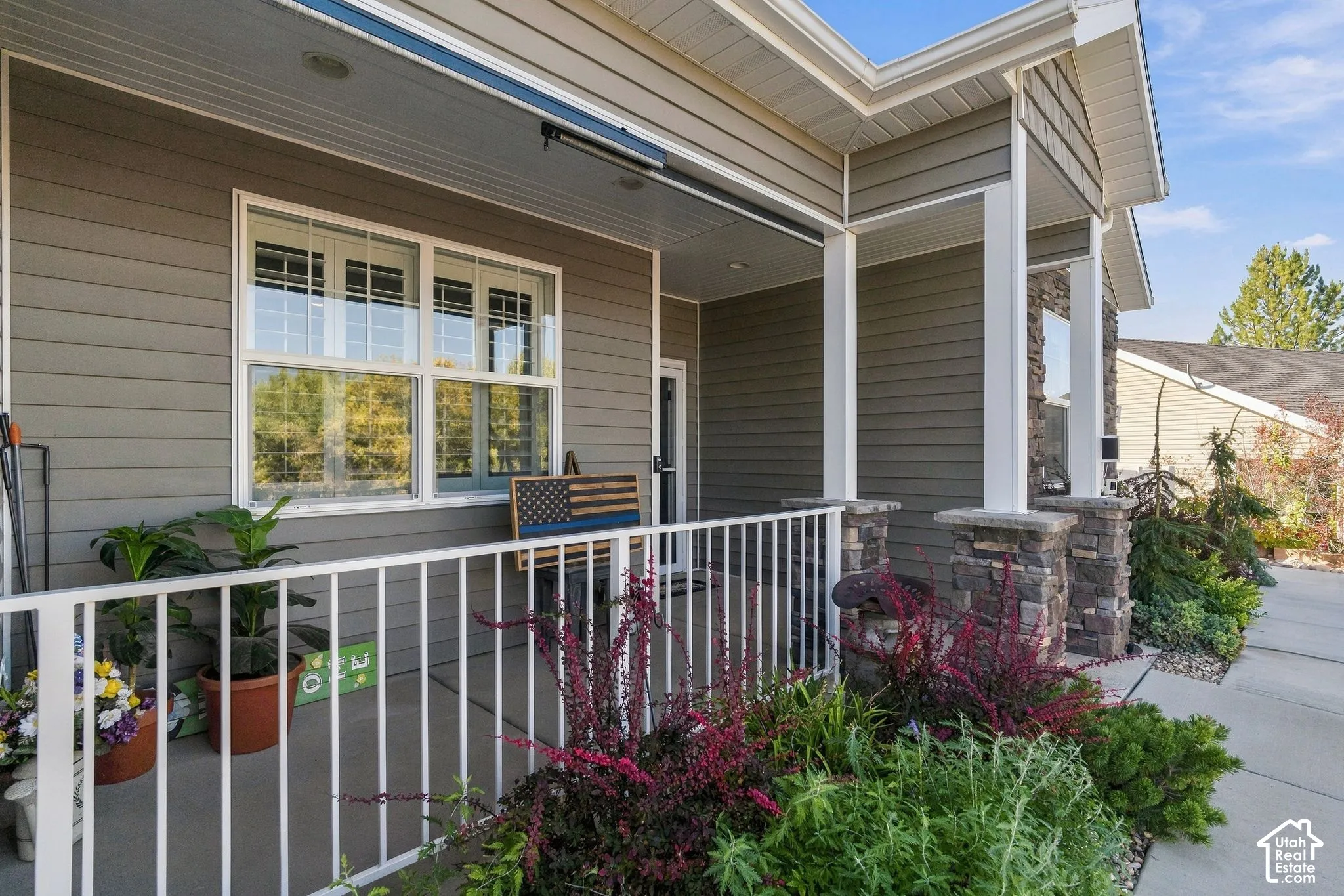 Covered front porch featuring white railing, stacked stone column bases, and horizontal siding