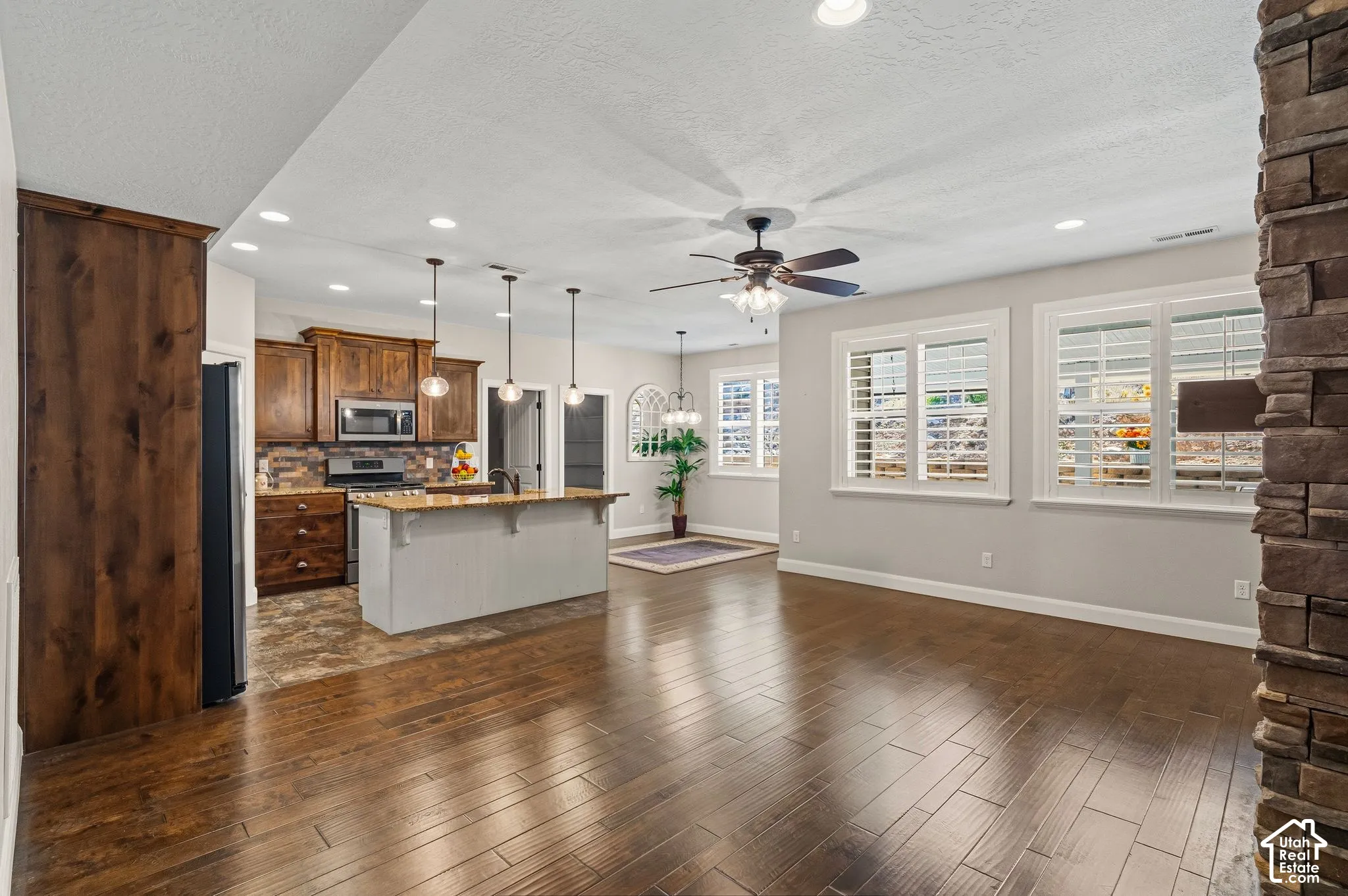 Open concept living area featuring dark wood-finish flooring, a stone accent wall, and multiple windows with plantation shutters
